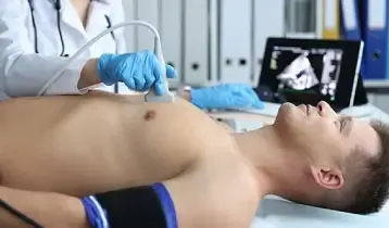 Médica fazendo ecocardiograma transtorácico em paciente deitado, com a imagem do coração no monitor