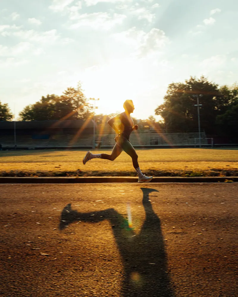 Corredor em disparada numa pista de atletismo ao entardecer, ilustrando o esforço físico avaliado no Teste Ergométrico