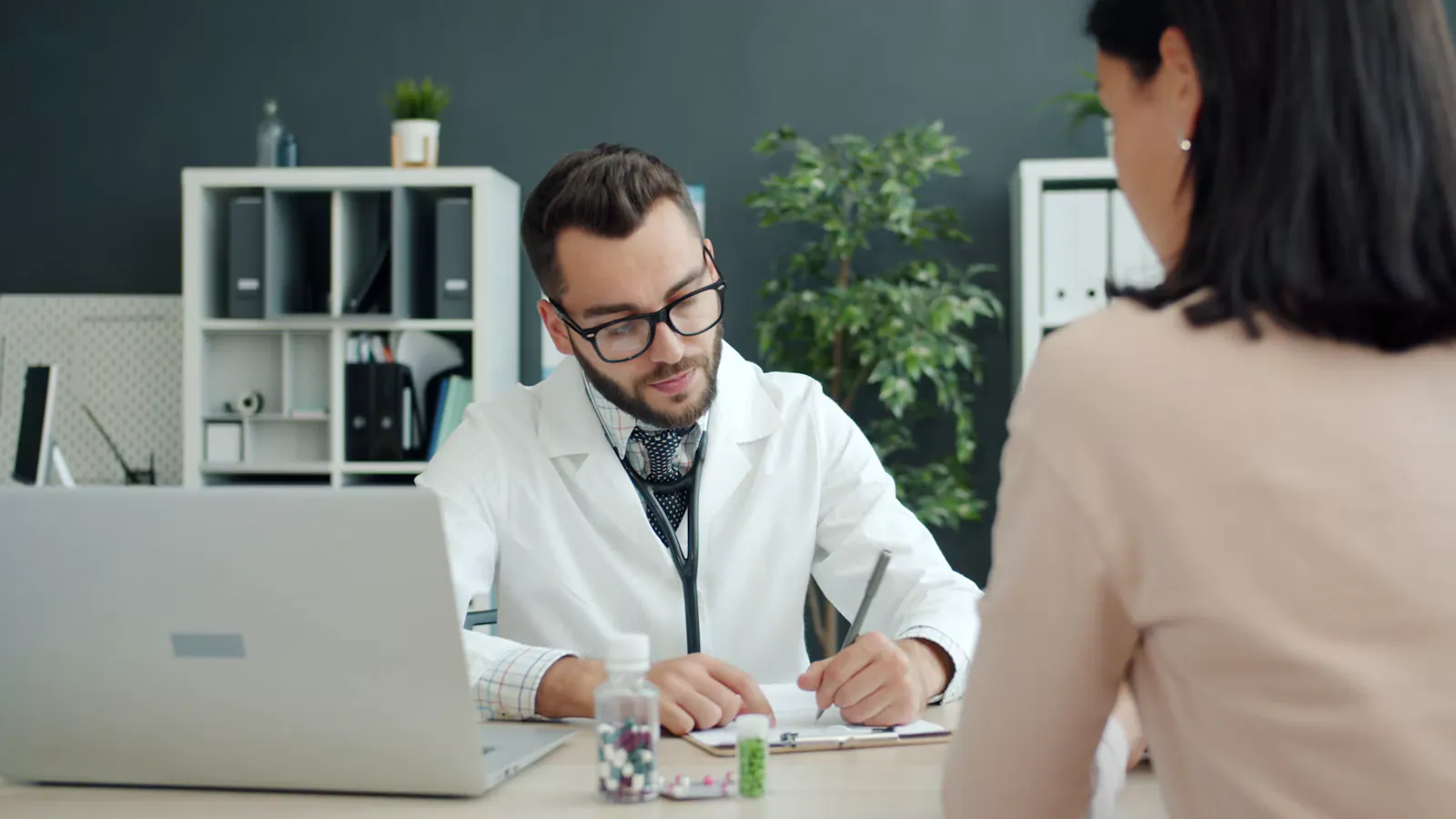 Médico de óculos fazendo anotações durante a consulta com uma paciente
