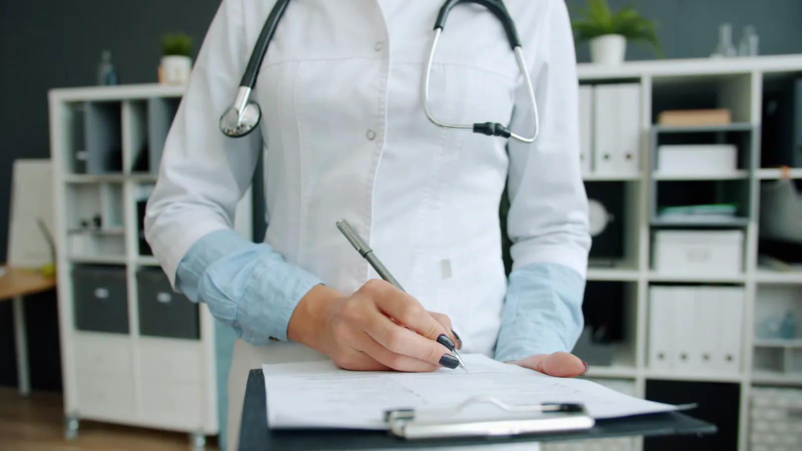 Médica com estetoscópio escrevendo em uma prancheta no consultório