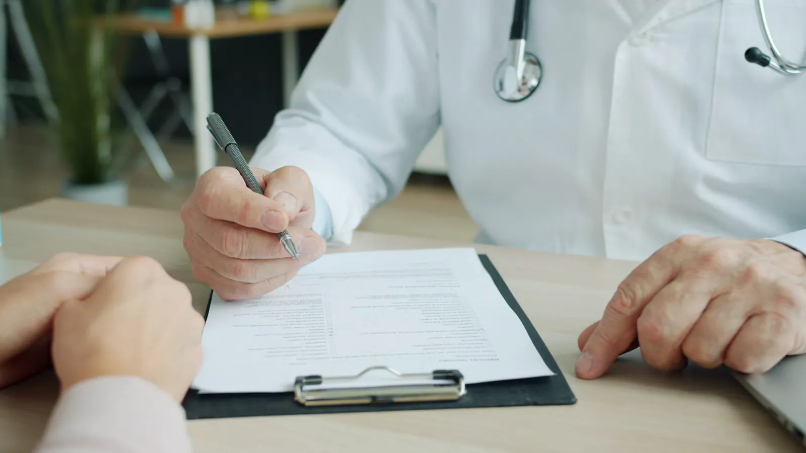 Médico de jaleco e estetoscópio preenchendo um formulário diante do paciente